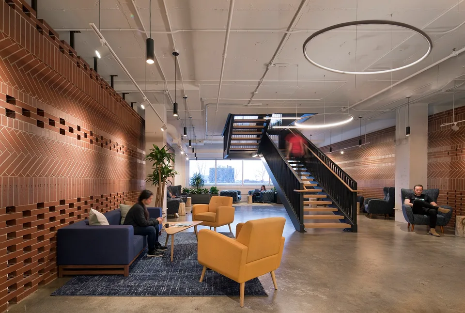 Element AI's shared workspace, with brick walls, yellow lounge chairs and a central staircase